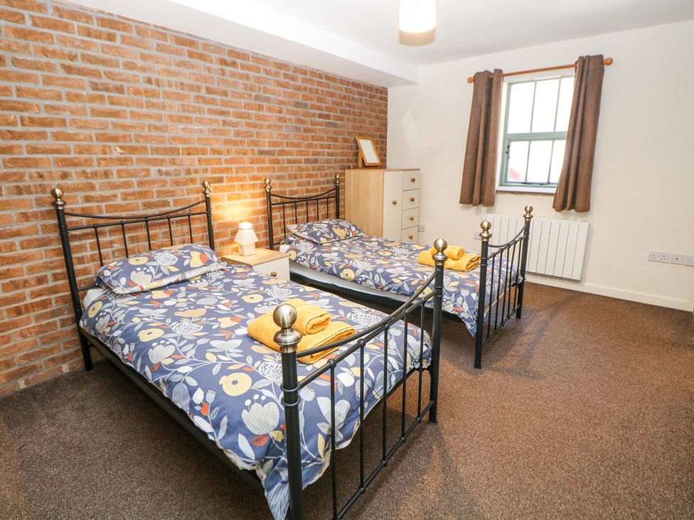 A bedroom with two single beds with floral bedding a brick wall a window with curtains and a bedside table at Woodlands in Cowdale near Buxton