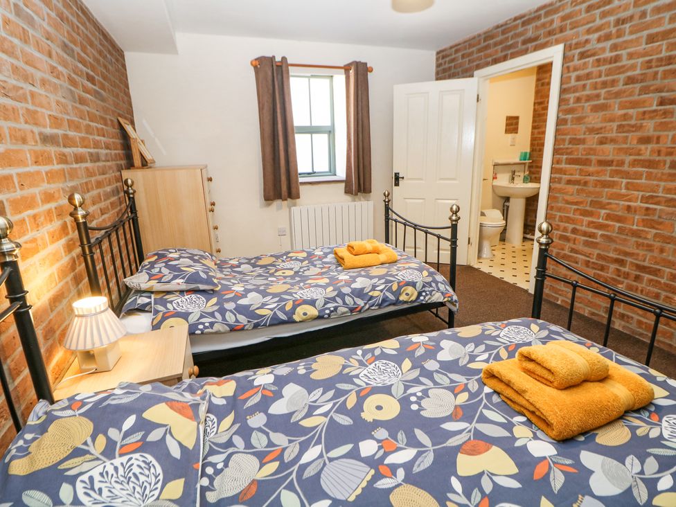 A bedroom with two single beds with floral bedding a wooden nightstand with a lamp a wooden dresser a window with curtains and an open door leading to a bathroom at Woodlands in Cowdale near Buxton