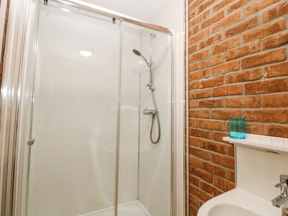 A shower enclosure with glass doors and a shower head beside a brick wall and a sink with a glass on the shelf at Woodlands in Cowdale near Buxton