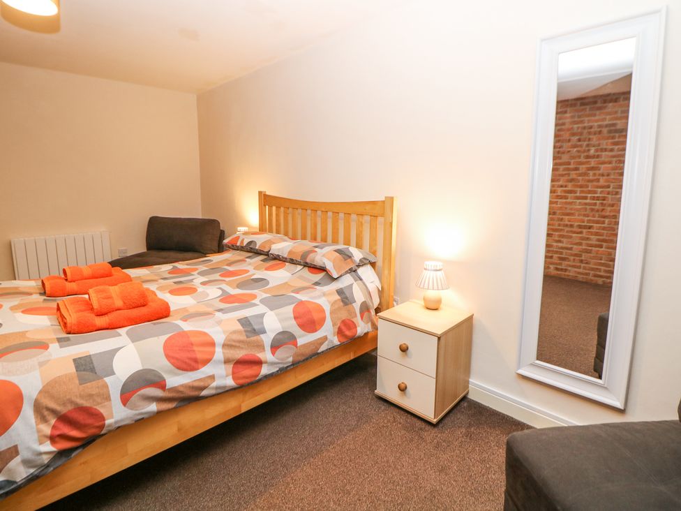 A bedroom with a wooden bed and geometric patterned bedding next to a nightstand with a lamp and a full length mirror at Woodlands in Cowdale near Buxton