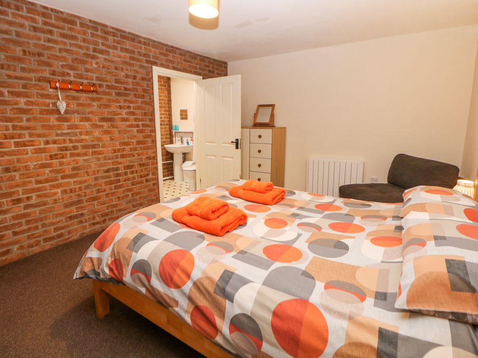 A bedroom with a bed with orange patterned bedding and folded orange towels a brick wall and an open door leading to a bathroom at Woodlands in Cowdale near Buxton