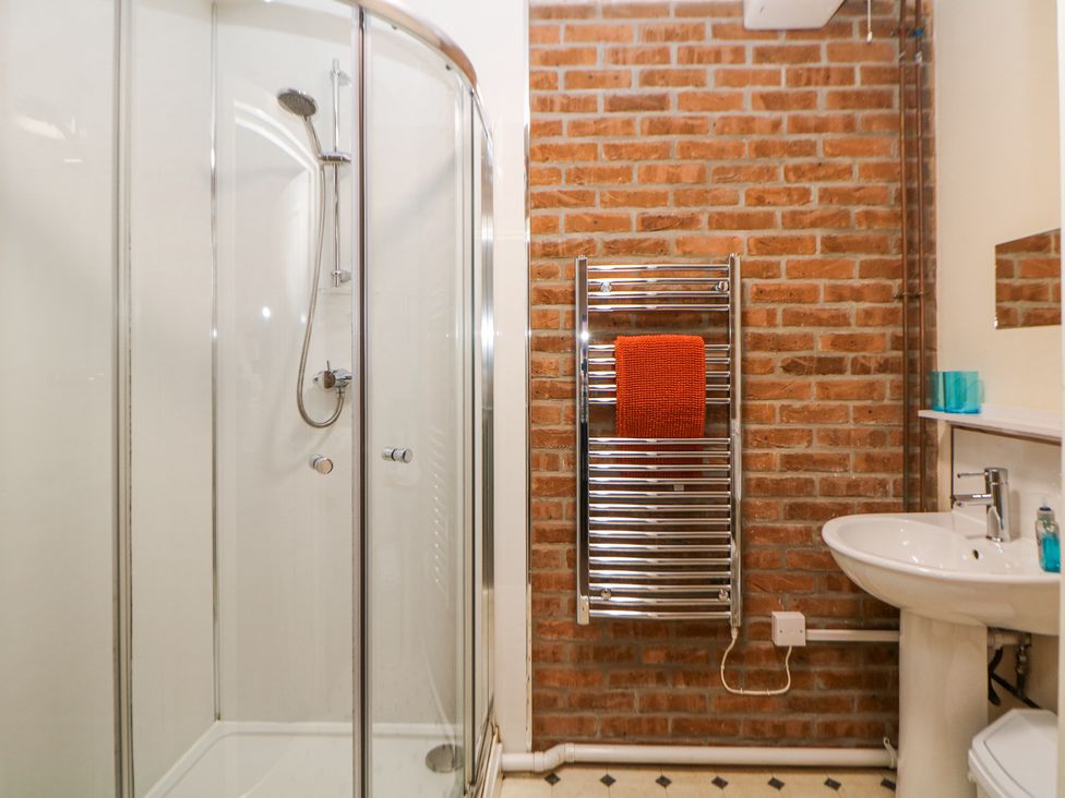 A bathroom with a glass shower enclosure a towel rack with an orange towel a sink and a mirror at Woodlands in Cowdale near Buxton