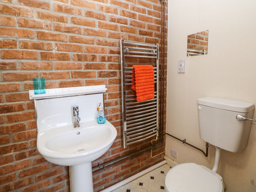 A bathroom with a white sink and toilet a heated towel rail with an orange towel and a brick wall at Woodlands in Cowdale near Buxton