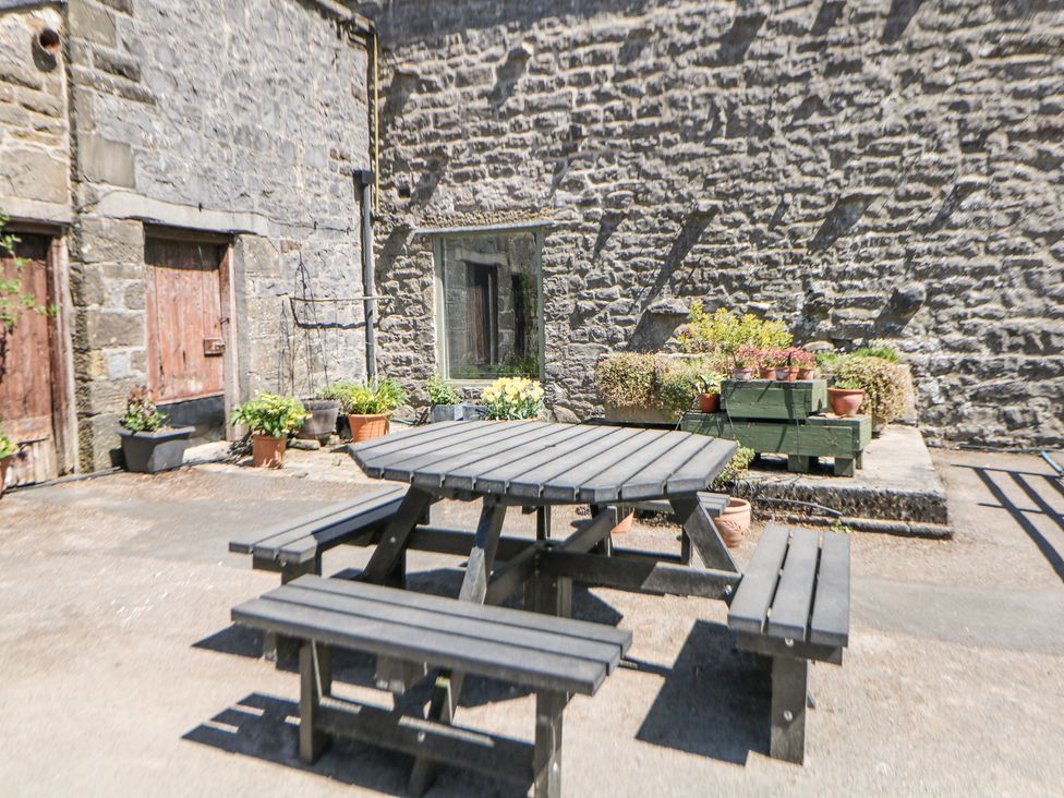 An outdoor stone patio area with a wooden picnic table and benches and potted plants against a stone wall at Woodlands in Cowdale near Buxton