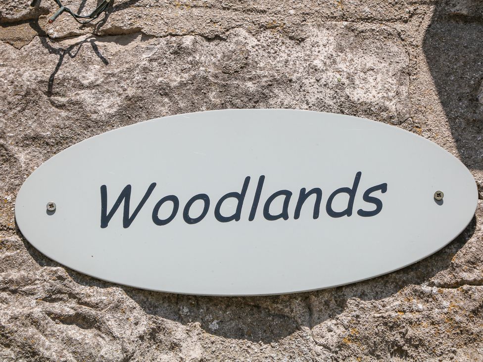 An oval white sign with the word Woodlands on a stone wall at Woodlands Cowdale near Buxton