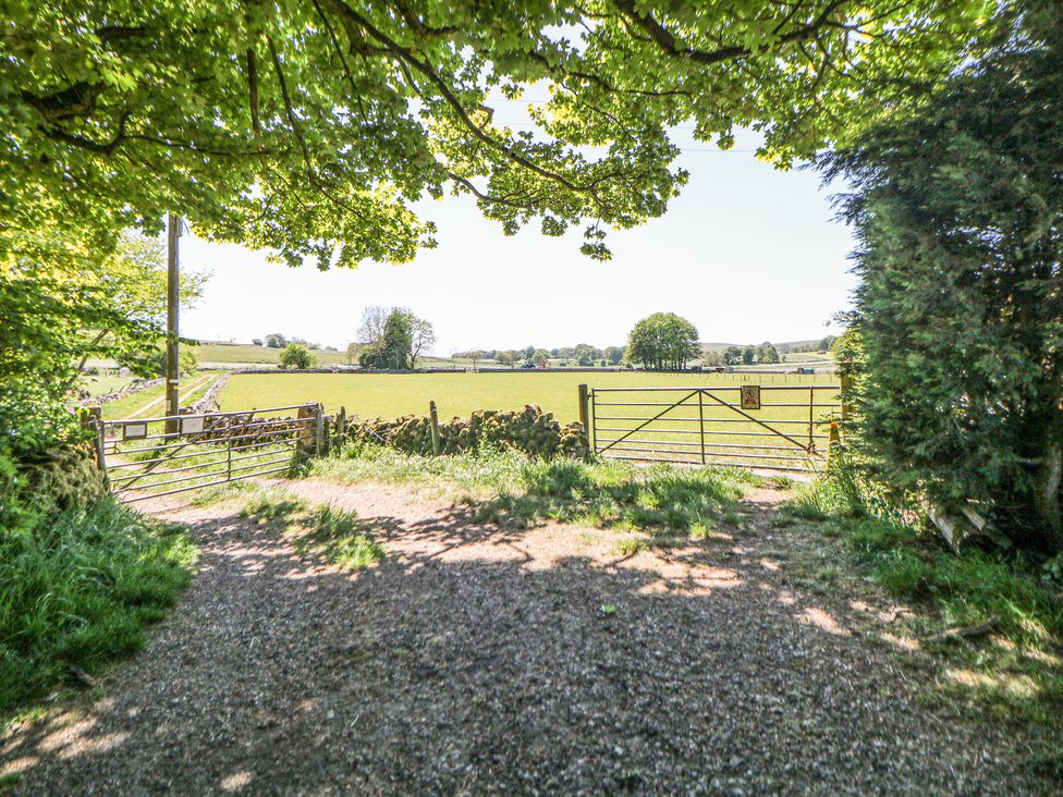 A gravel pathway leading to two metal gates opening to green fields with trees in the distance at Woodlands in Cowdale near Buxton