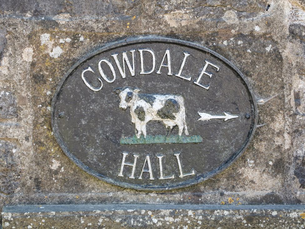 A stone wall with an oval sign of a cow and an arrow at Cowdale near Buxton