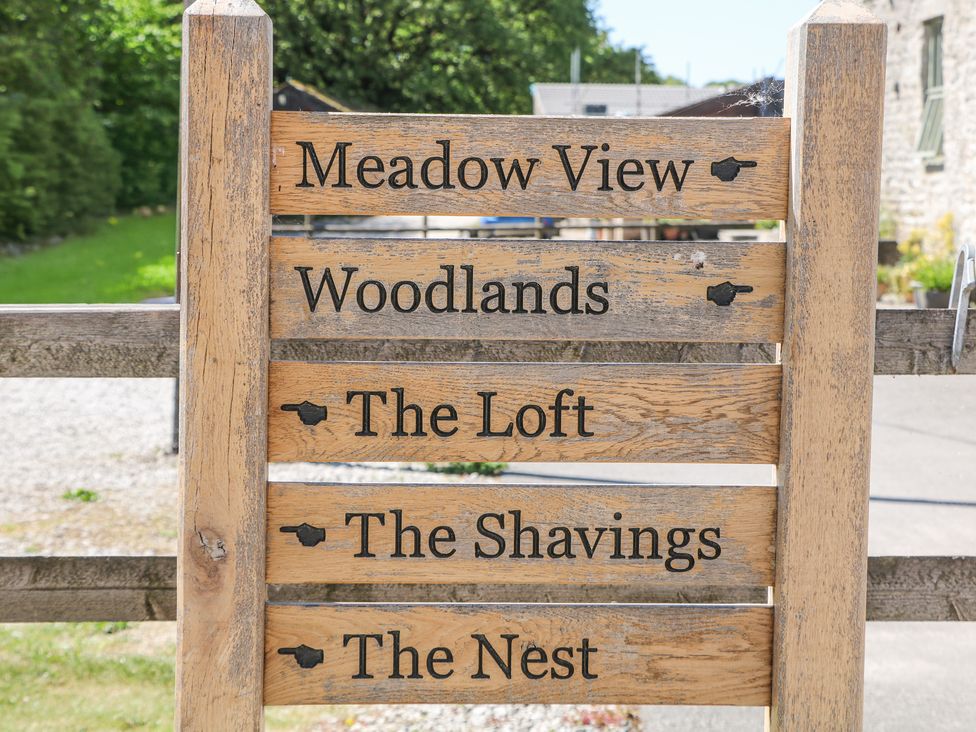 A wooden signpost with black text and arrows pointing to Meadow View Woodlands The Loft The Shavings and The Nest at Woodlands in Cowdale near Buxton