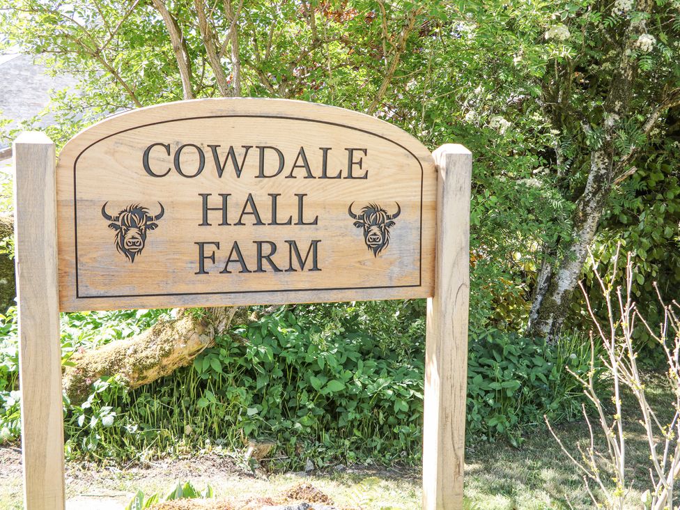 A wooden sign for Cowdale Hall Farm with greenery and trees behind it at Woodlands in Cowdale near Buxton