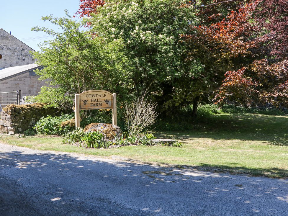 An outdoor scene with a Cowdale Hall Farm sign near a gravel road and surrounded by trees and plants at Woodlands in Cowdale near Buxton