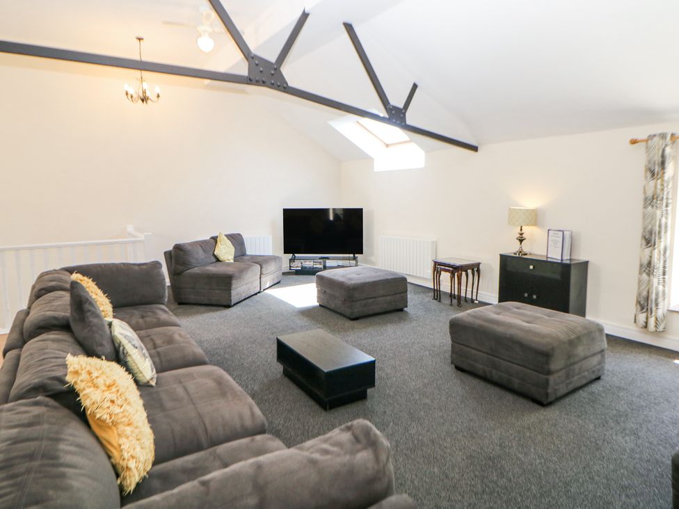 A living room with gray sofas and ottomans a black coffee table and a flat screen tv at Meadow View in Buxton
