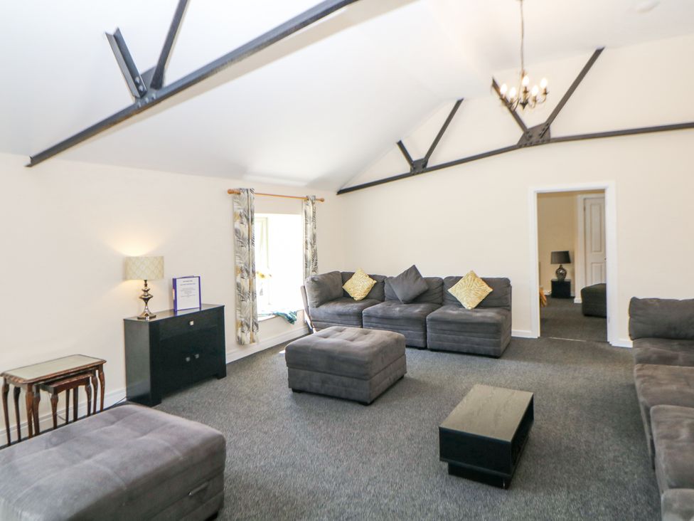 A living room with gray sofas and ottomans a black cabinet with lamp and a small table at Meadow View in Buxton