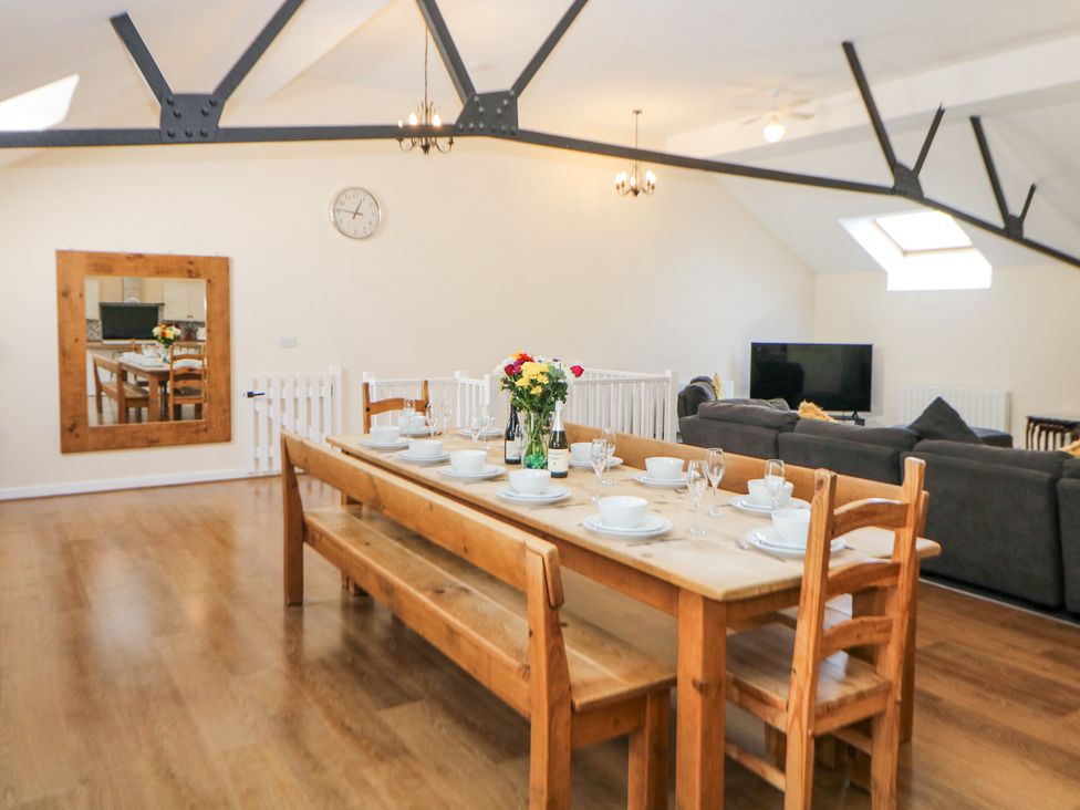 A dining table set with dishes and glasses beside a living area with sofas and a TV at Meadow View in Buxton