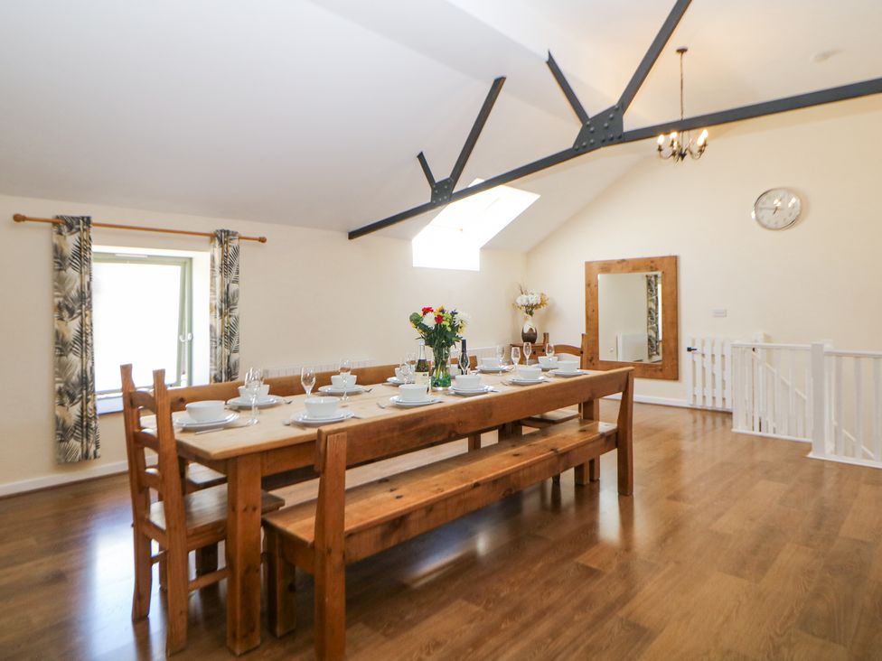 A dining room with a wooden table and benches set for a meal with plates glasses and flowers at Meadow View in Buxton