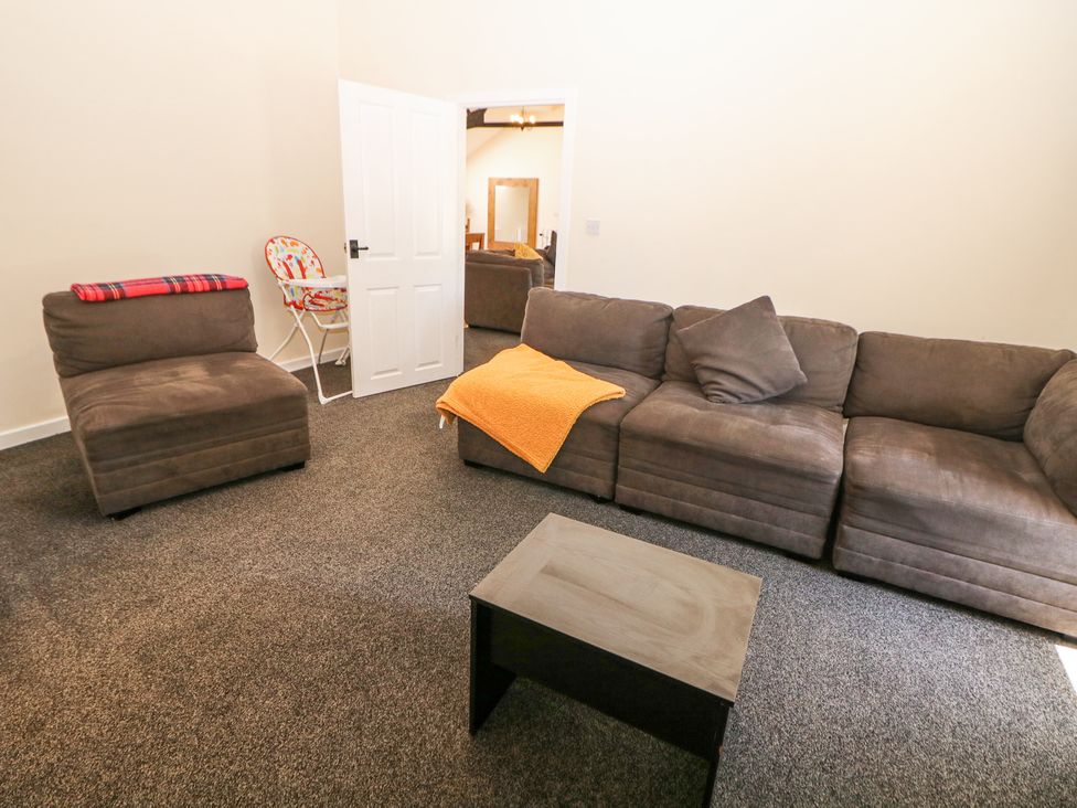 A living room with a brown sofa and chair a small wooden table and a baby high chair at Meadow View in Buxton