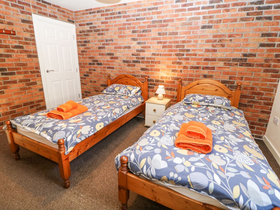 A bedroom with two single wooden beds with floral bedding and orange towels on them a white nightstand with a lamp between the beds at Meadow View in Buxton
