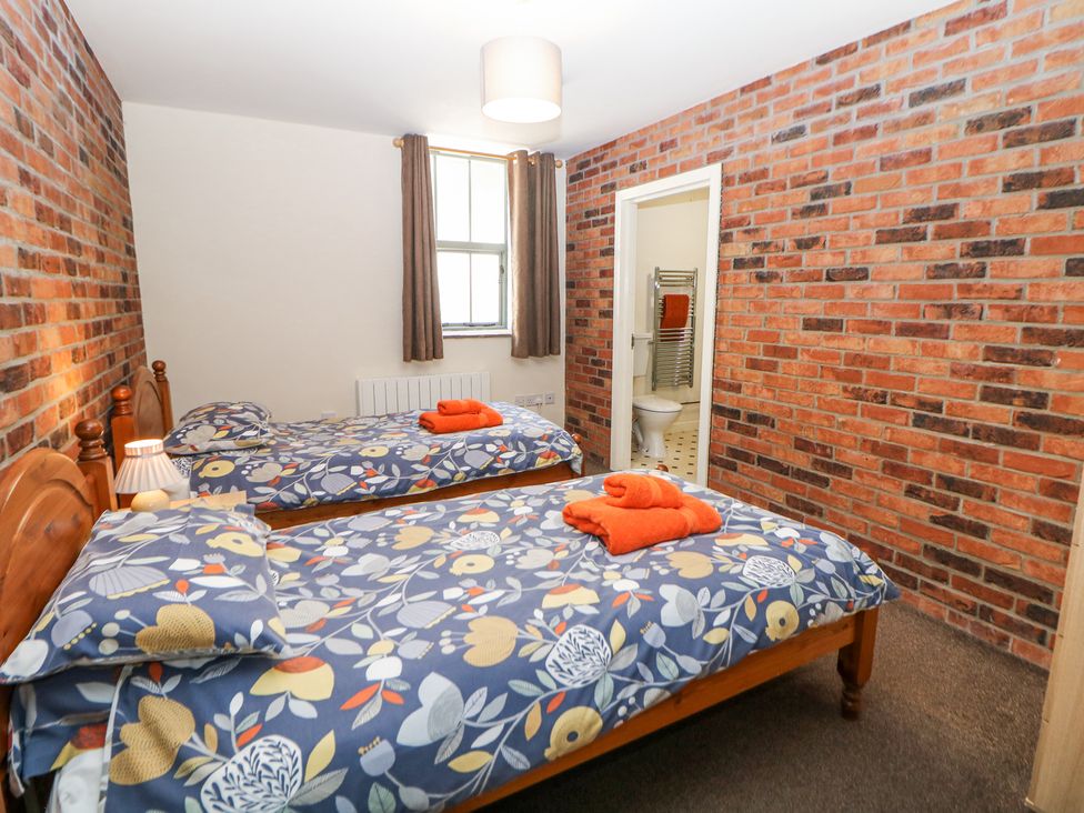 A bedroom with two single beds with floral bedding and orange towels a small lamp on a bedside table and an en suite bathroom at Meadow View in Buxton