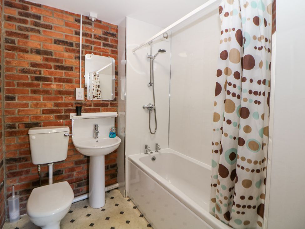 A bathroom with a toilet, pedestal sink, mirror, bathtub with shower and a patterned shower curtain at Meadow View in Buxton