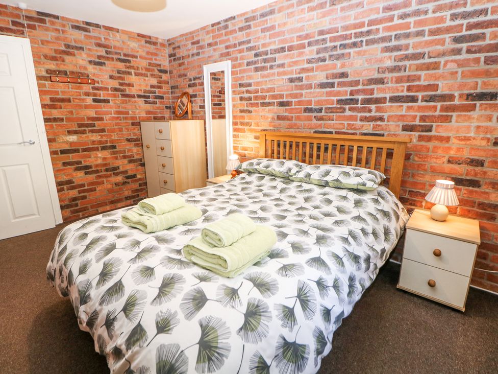 A bedroom with a wooden bed frame with patterned bedding two bedside tables with lamps a chest of drawers a full length mirror and exposed brick walls at Meadow View in Buxton