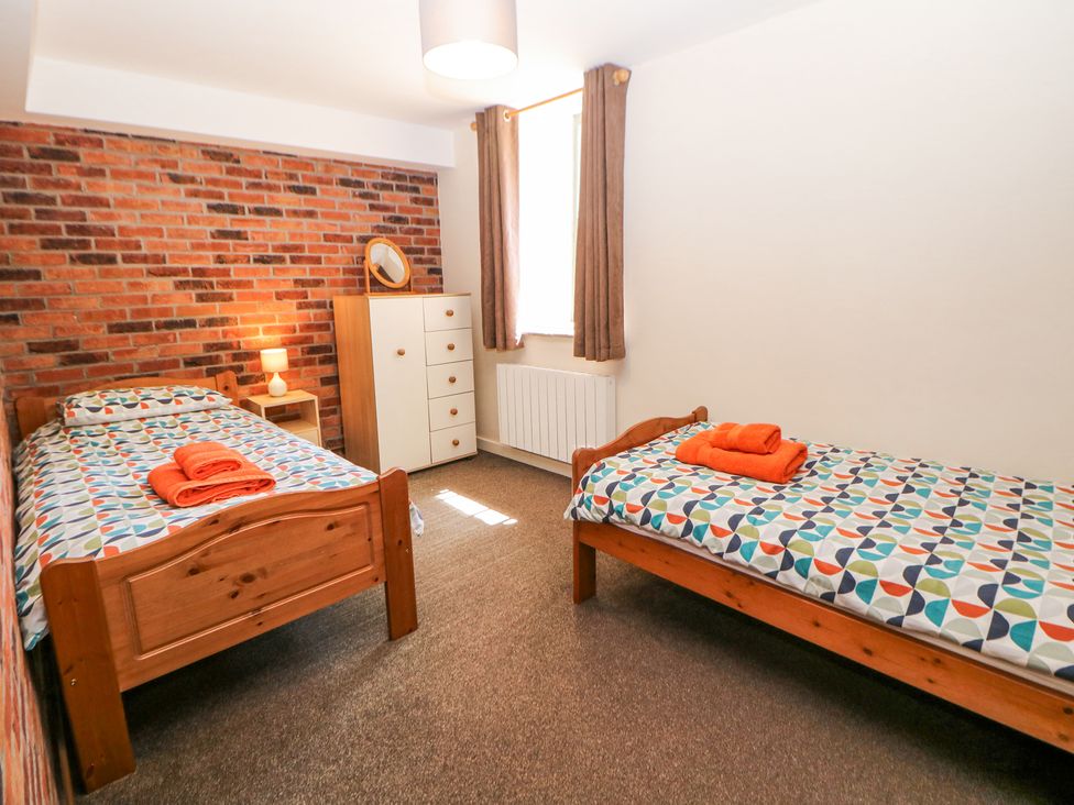 A bedroom with two single wooden beds with patterned bedding and orange towels a lamp a window with curtains and a dresser against a brick wall at Meadow View in Buxton