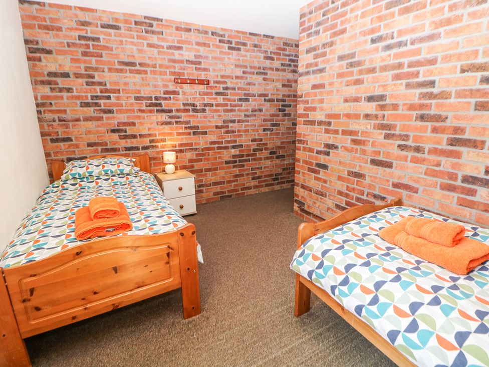 A bedroom with two single wooden beds orange towels on the beds a nightstand with a lamp and brick walls at Meadow View in Buxton