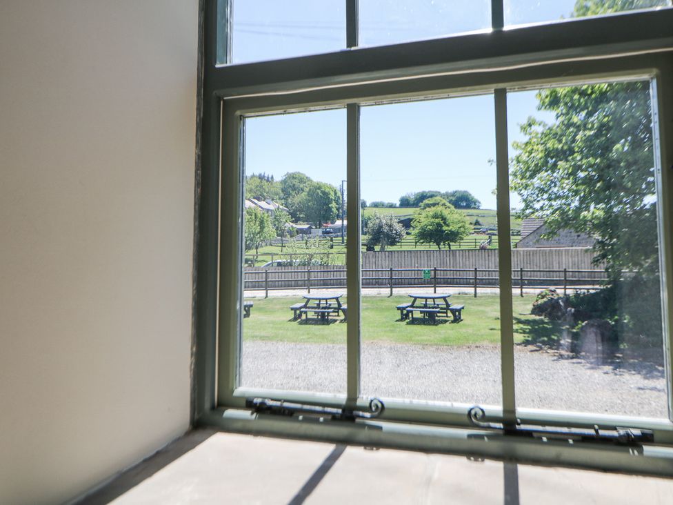 A window view of outdoor picnic tables on grass with a fenced area and trees at Meadow View in Buxton