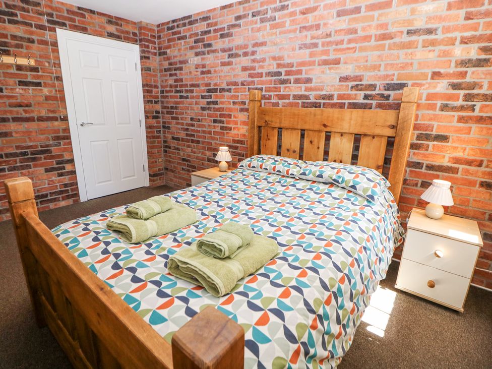 A bedroom with a wooden bed patterned bedspread green towels on the bed beside wooden bedside tables with lamps at Meadow View in Buxton