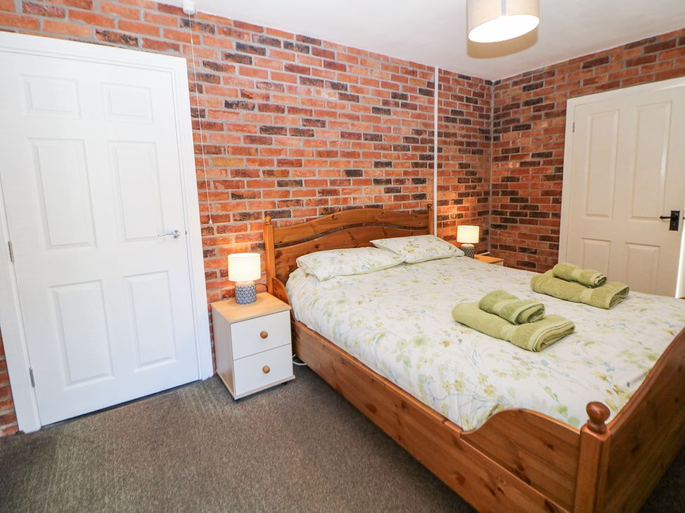 A bedroom with a wooden bed with floral bedding two bedside tables with lamps and brick walls at Meadow View in Buxton
