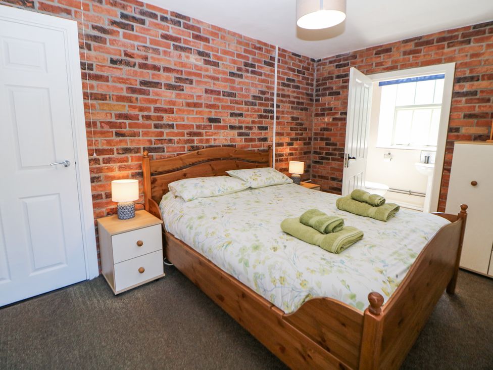 A bedroom with a wooden bed with floral bedspread two bedside tables with lamps and an open door leading to a bathroom at Meadow View in Buxton