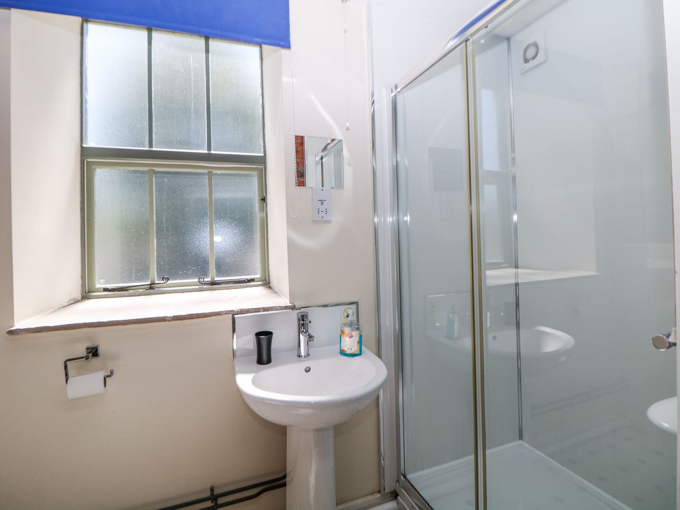 A bathroom with a pedestal sink a glass-enclosed shower window with a blue blind and a toilet paper holder at Meadow View in Buxton