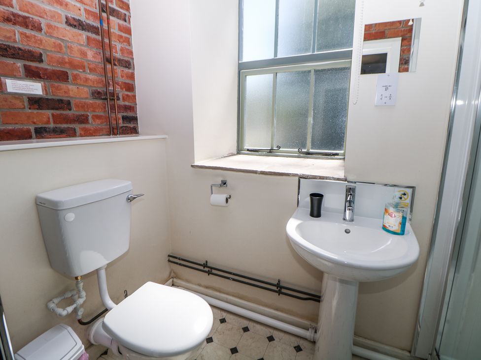 A bathroom with a toilet a pedestal sink a window and red brick wall at Meadow View in Buxton