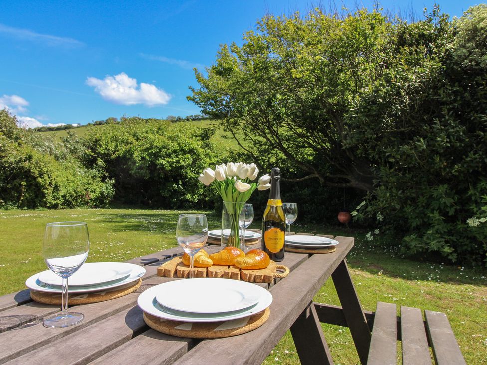 A table set with plates, glasses, and flowers in an outdoor dining area at 4 Thornlea Mews Hope Cove