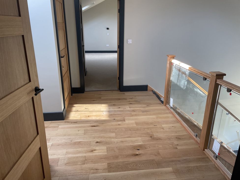 A hallway with wooden flooring and doors leading to rooms at 1 New Dairy Barn