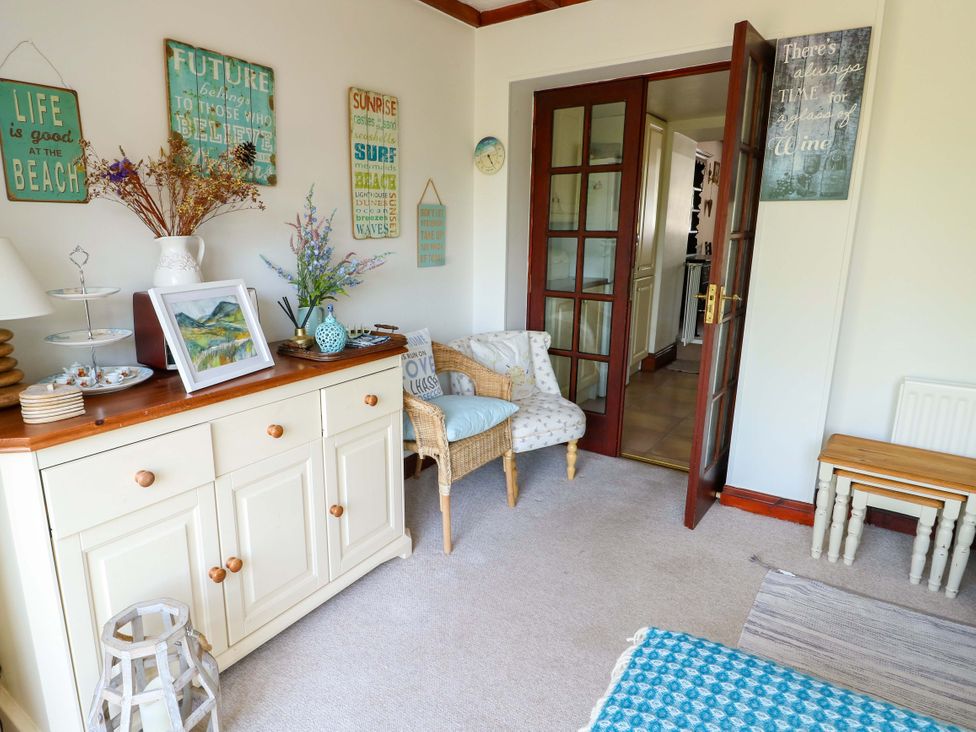 A snug with a cabinet, armchair, and decorative items at Bryn Pydew in Llandudno Junction