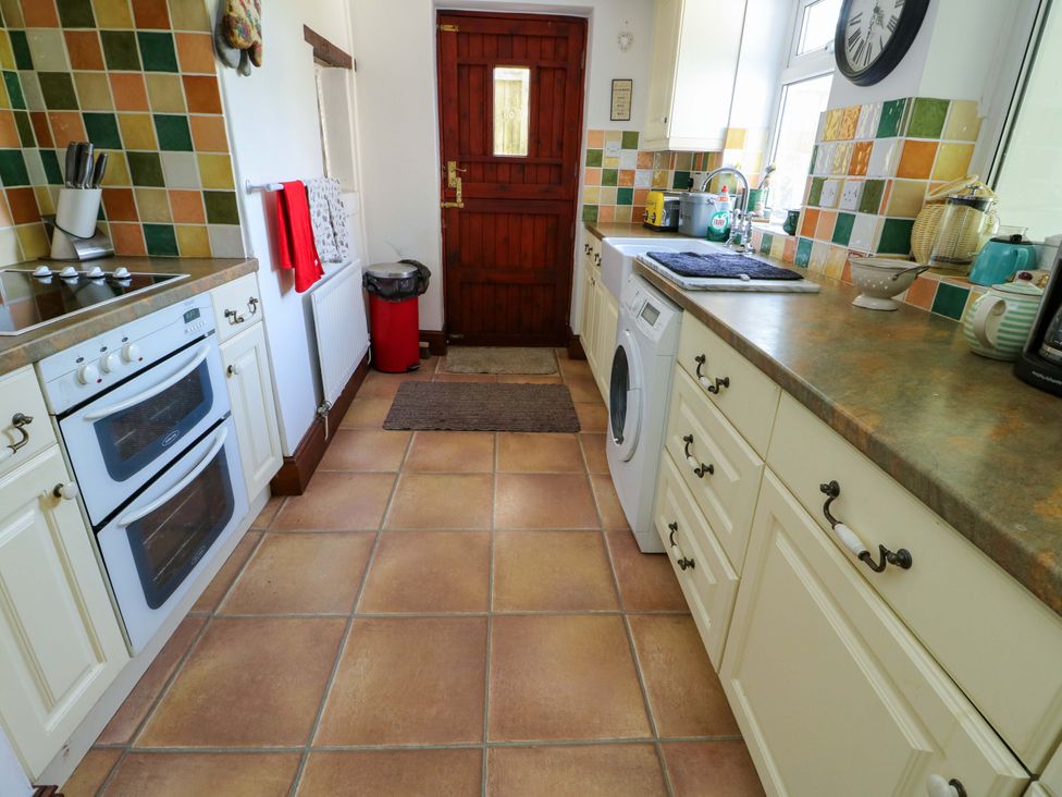 A kitchen with oven, sink, washing machine and door at Bryn Pydew in Llandudno Junction