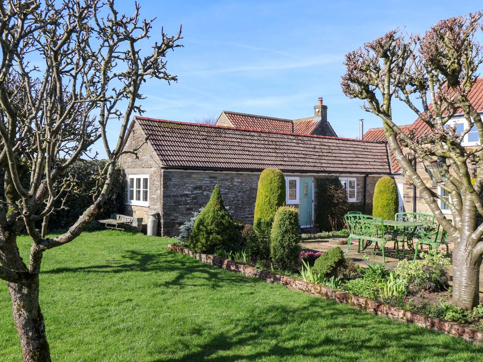 A garden with a stone building and seating area at Cartwheel Cottage in Yearsley