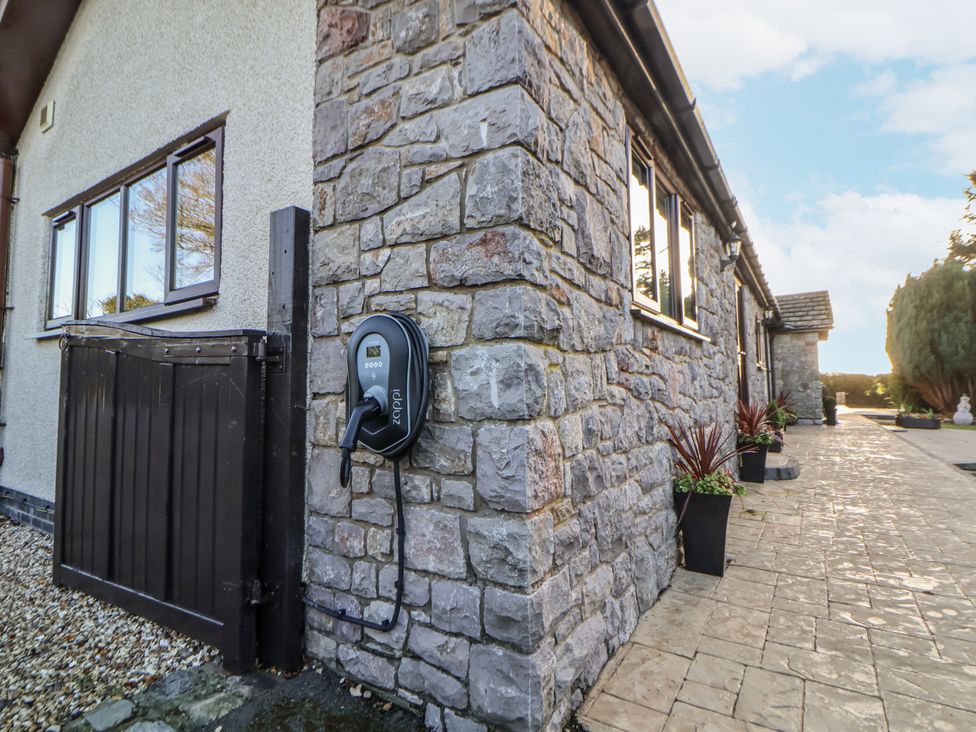 An outdoor area with an electric vehicle charger and stone wall at Arosfa in Axton near Trelawynd