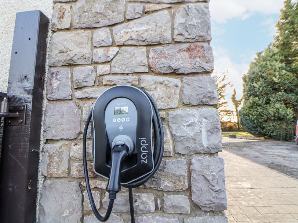 An electric vehicle charger mounted on a stone wall at Arosfa Axton near Trelawynd