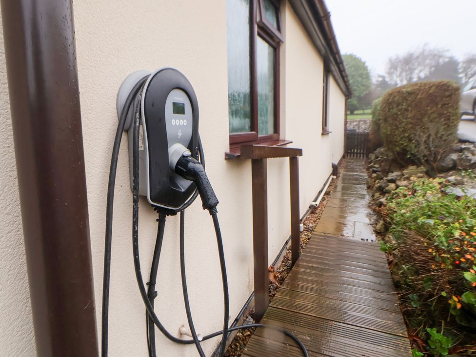 An electric vehicle charger mounted on a wall near a pathway at Arosfa in Axton near Trelawynd