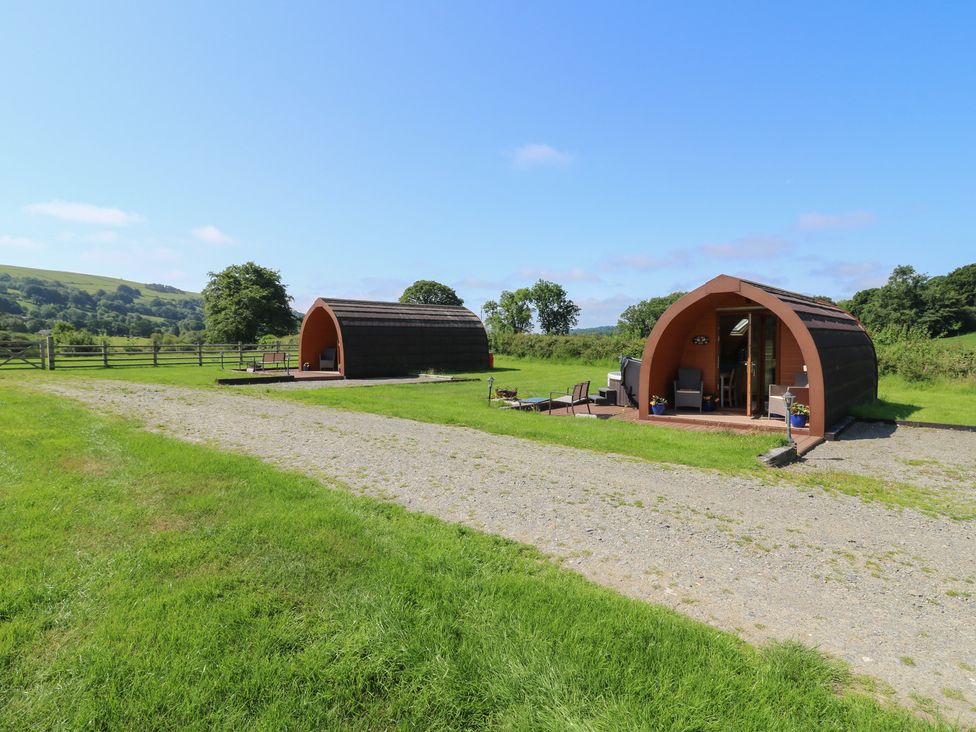 Two glamping pods with outdoor seating in a grassy area at Bwthyn Bach Brefi