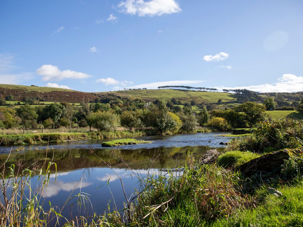 A river surrounded by trees and hills at Bwthyn Bach Brefi
