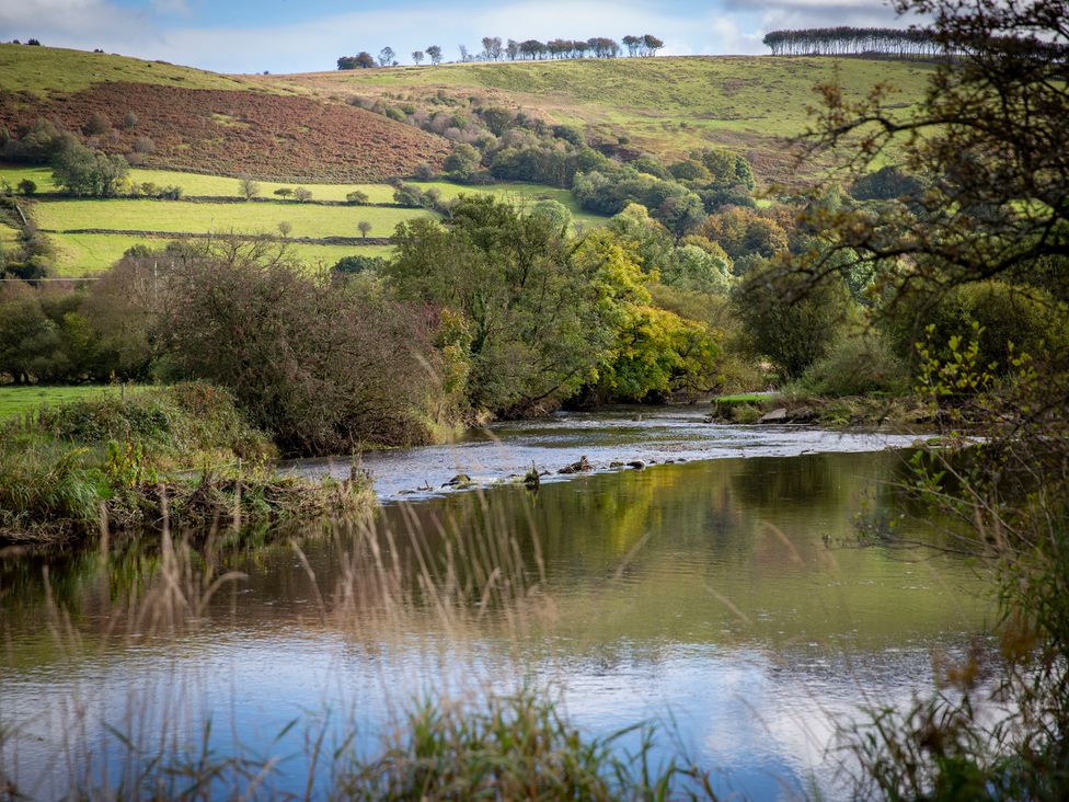 A river surrounded by trees and hills at Bwthyn Bach Brefi