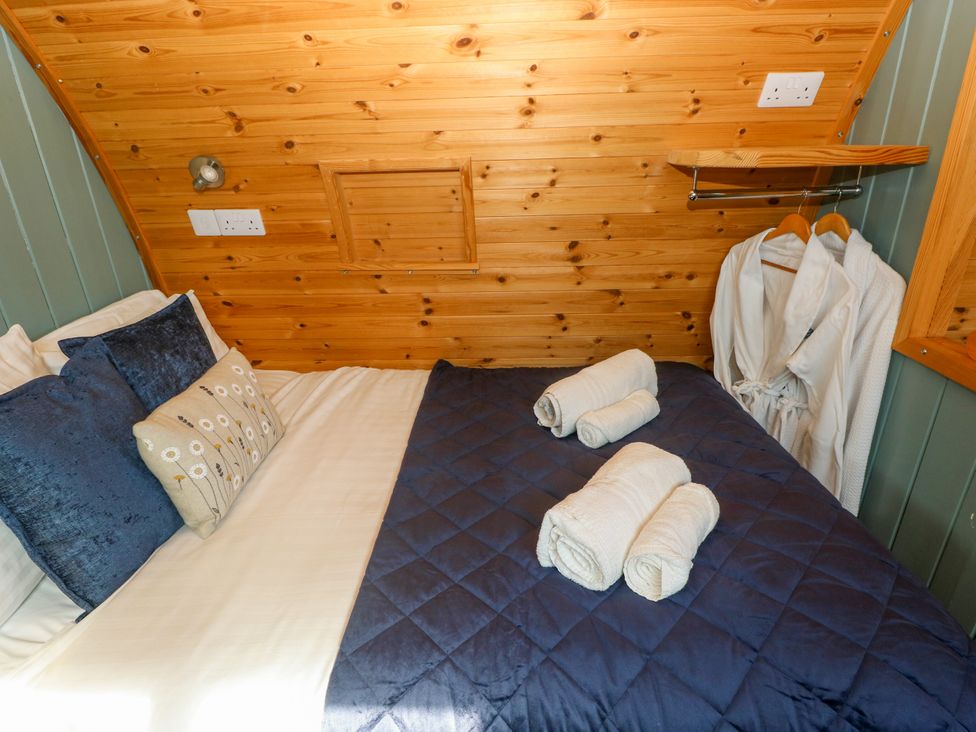 A bedroom with a bed, pillows, towels and a robe at Bwthyn Bach Brefi in Llanddewi-Brefi