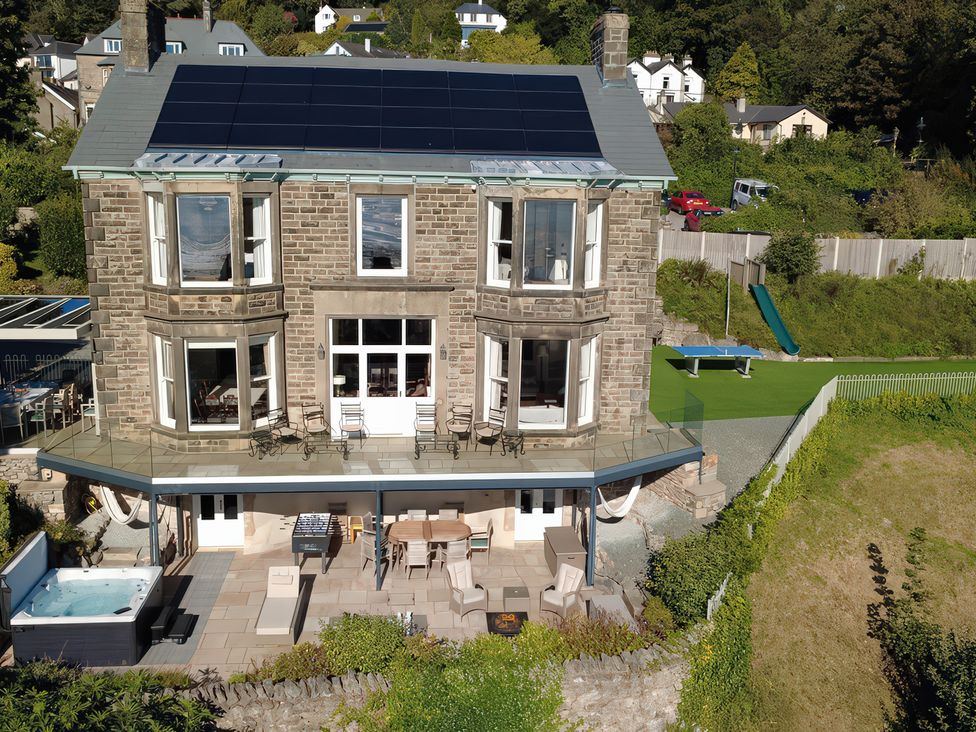 An outdoor area with a house, spa, dining table and lawn at Victoria Mount in Grange-Over-Sands
