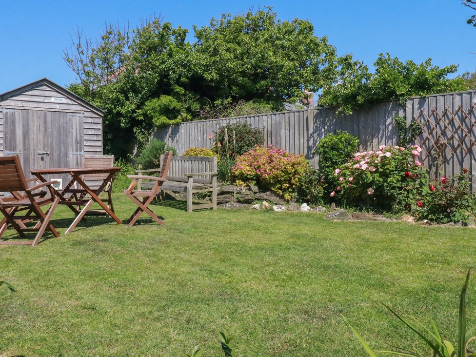 A garden with chairs and a table overlooking flower beds at Cove Cottage Tintagel