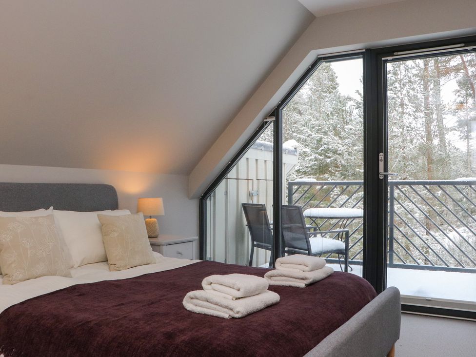 A bedroom with a bed and balcony view at Wildcat Lodge in Feshiebridge near Aviemore