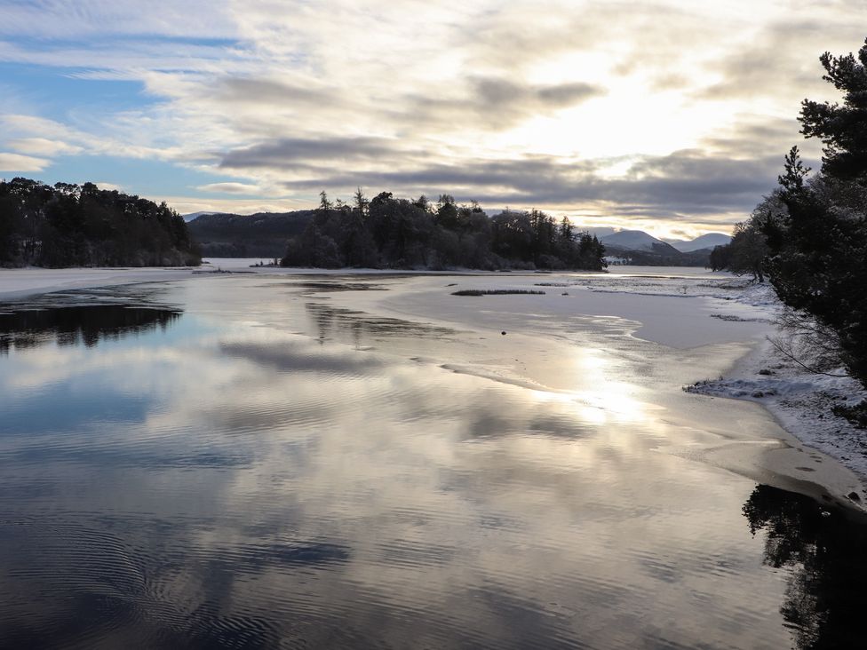 A landscape featuring water, trees, and mountains at Wildcat Lodge in Feshiebridge near Aviemore