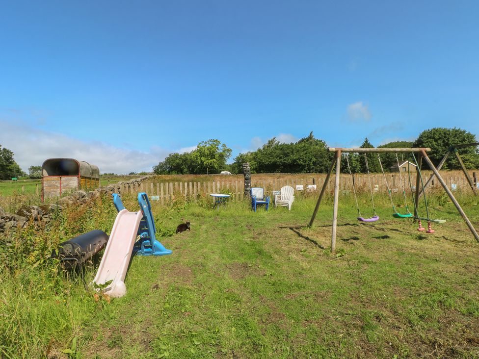 An outdoor area with a slide, swings, and plastic chairs at Moldy Warp Barn in Haworth
