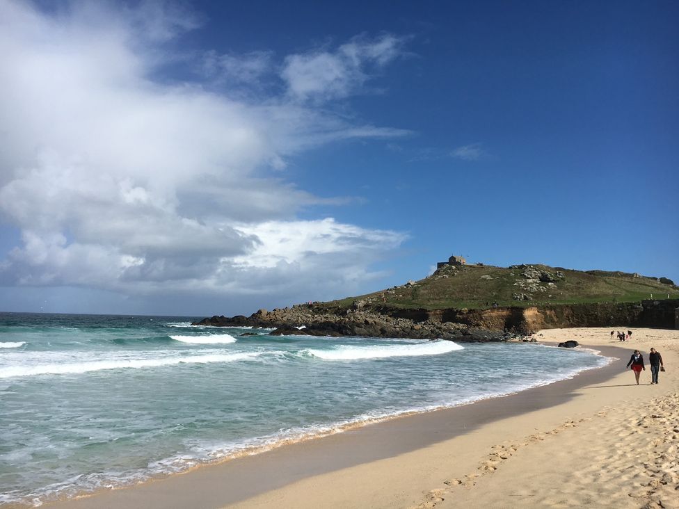 A beach scene with waves and people walking at Stargazy Cottage Praa Sands