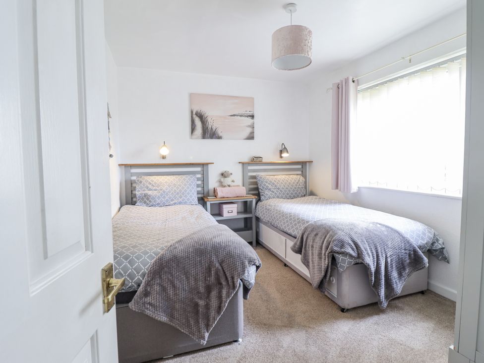 A bedroom with two beds and a bedside table at 8 Glan Ysgethin in Barmouth